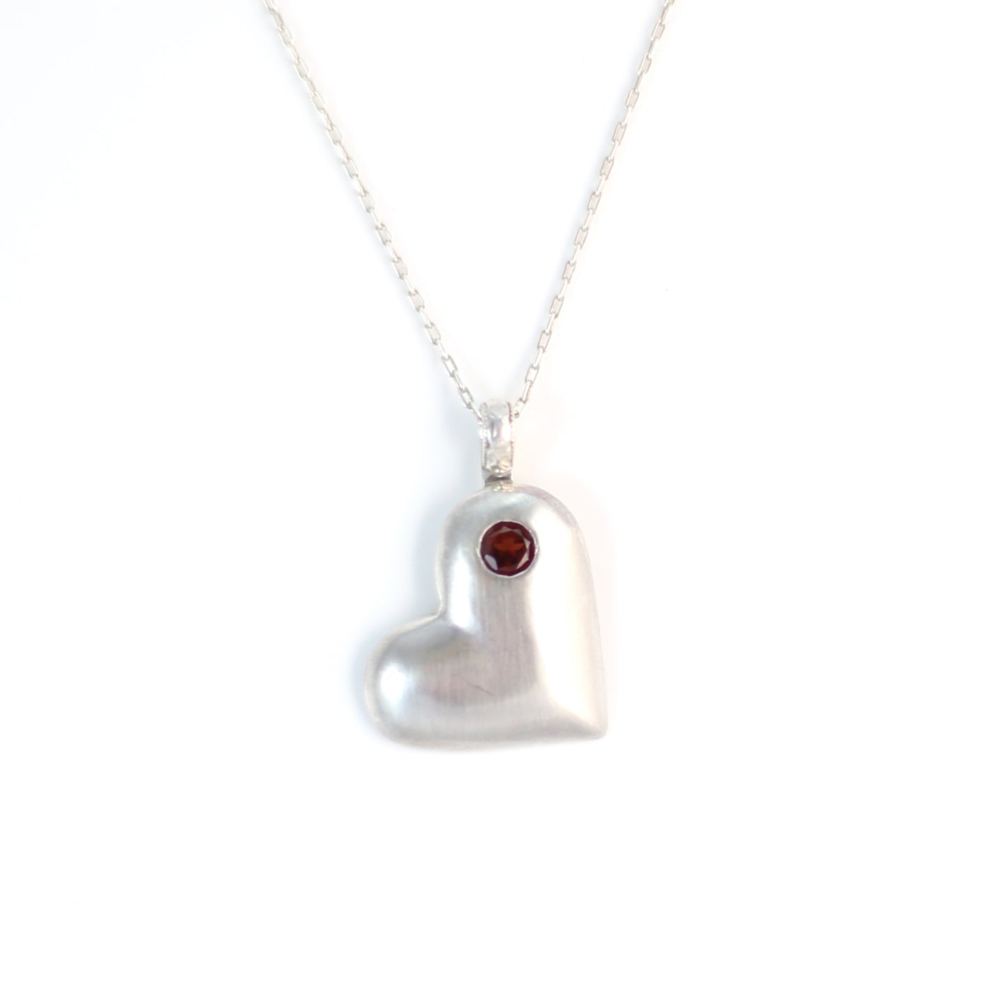 Handmade sterling silver offset heart pendant necklace with faceted natural red garnet gemstone. One of a kind by Cara Carter Jewelry