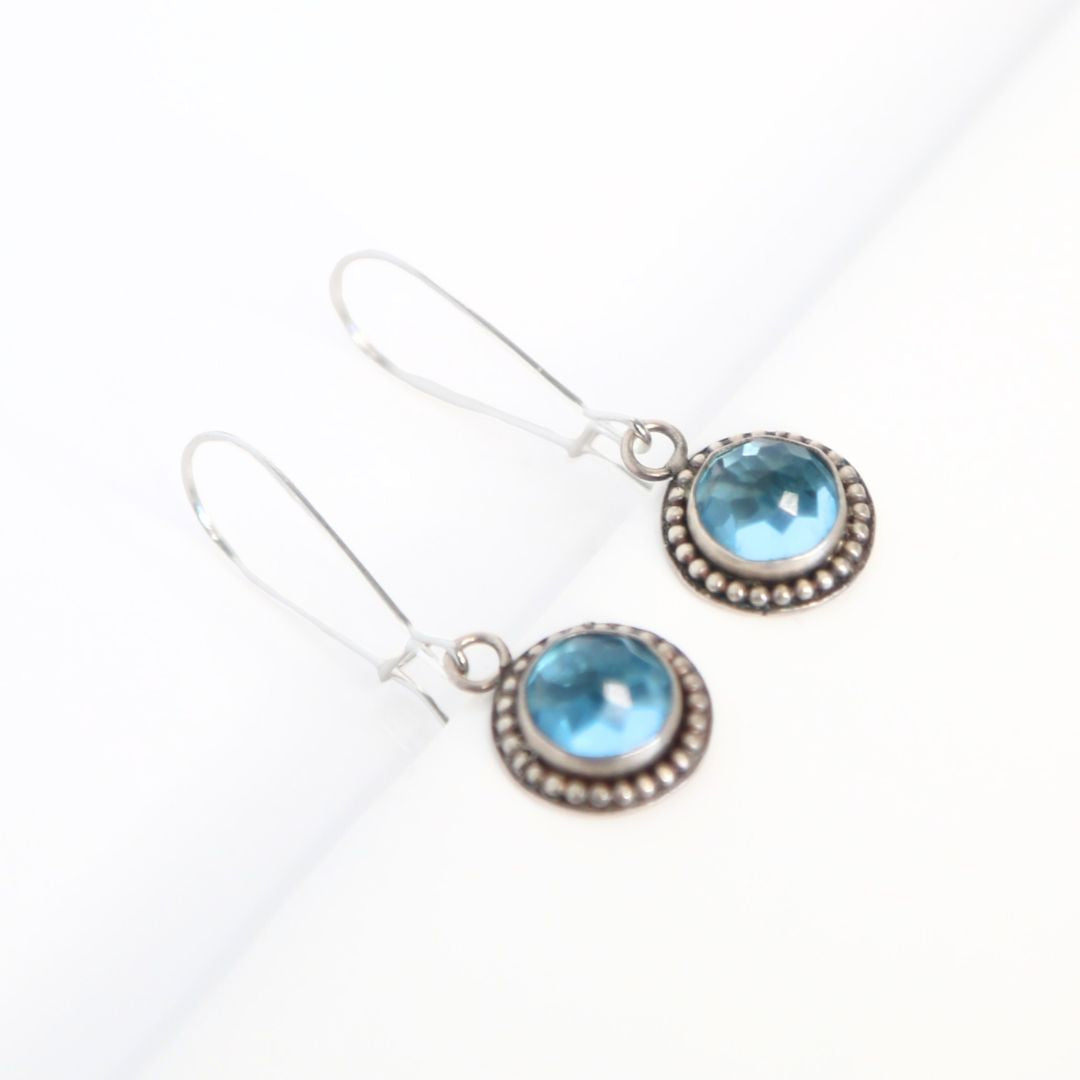 Handmade earrings featuring Swiss Blue Topaz faceted round gemstones set in sterling silver with beaded surround and long kidney hook earwires. By Cara Carter Jewelry