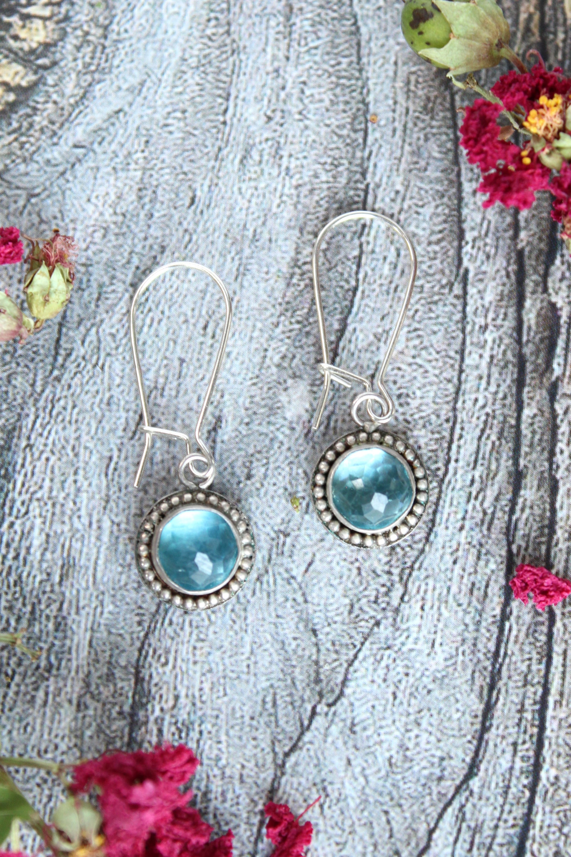 Handmade earrings featuring Swiss Blue Topaz faceted round gemstones set in sterling silver with beaded surround and long kidney hook earwires. By Cara Carter Jewelry